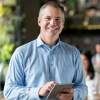 Smiling businessman holding a tablet in a modern office setting, representing professional technology use and workplace collaboration.