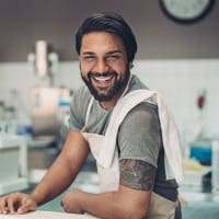 Smiling male chef in a kitchen, wearing an apron and showcasing a warm, welcoming demeanor, perfect for a restaurant or culinary blog.