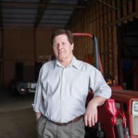 Man standing next to a red tractor in a barn, showcasing agricultural machinery and farming expertise.